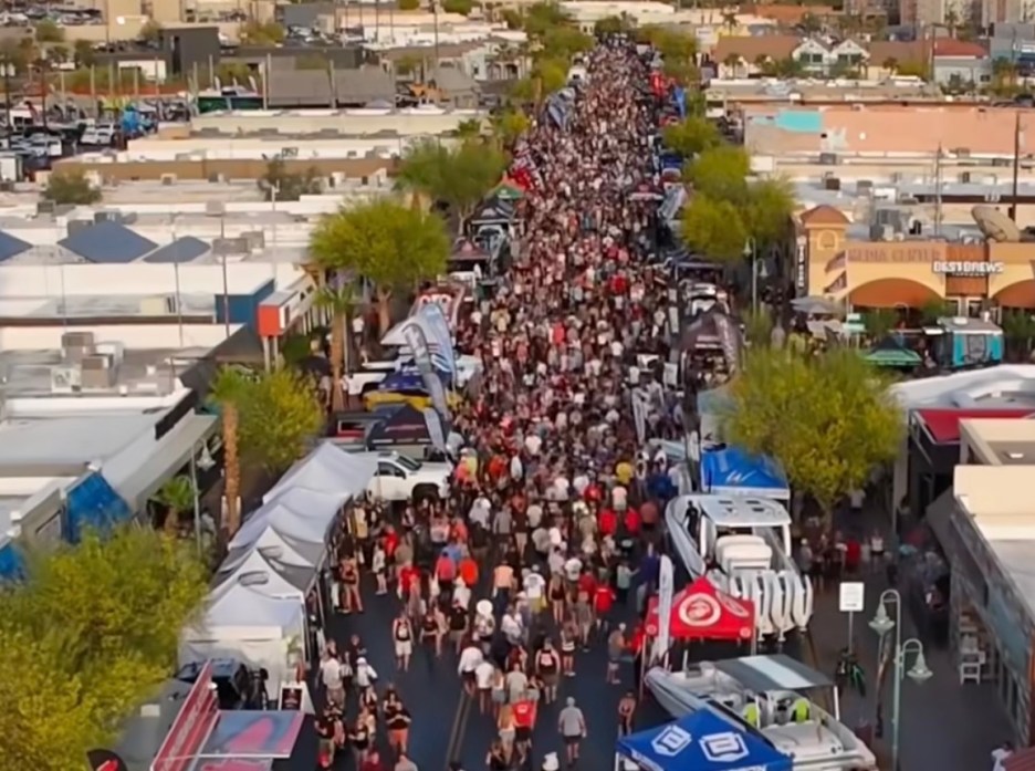Aerial view of a crowded street filled with people walking, surrounded by vendor tents and parked vehicles.