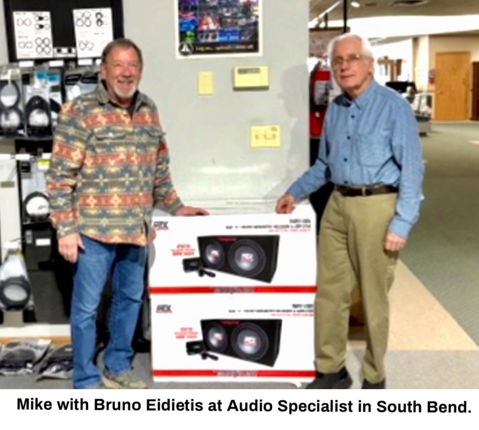 Two men standing next to two audio speaker boxes at a retail store.