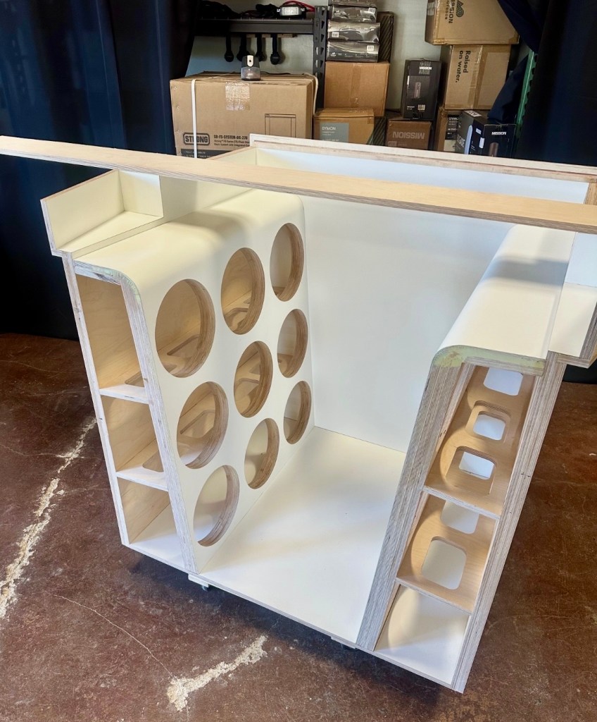 A partially assembled wooden structure with multiple circular cutouts and compartments, designed for storage or display.