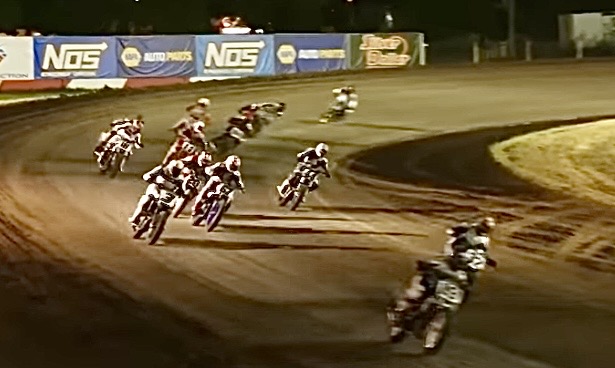A group of motorcycle racers competing on a dirt track during a night race.