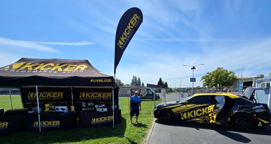 A promotional tent and display for Kicker Performance Audio at an outdoor event, featuring audio equipment and a car wrapped in Kicker branding.