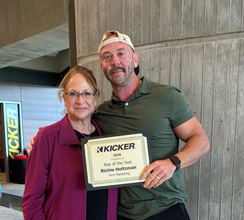 A woman in a purple jacket and glasses stands next to a man in a green shirt holding an award certificate that reads 'Rep of the Year' presented to Richie Holtzman for Tech Marketing.